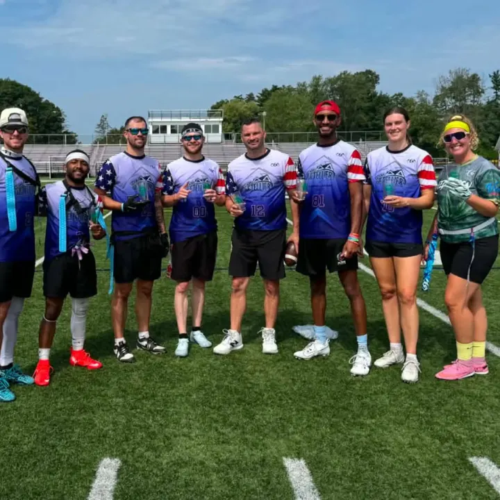 A coed squad in stars-and-stripes jerseys on the turf, holding small trophies